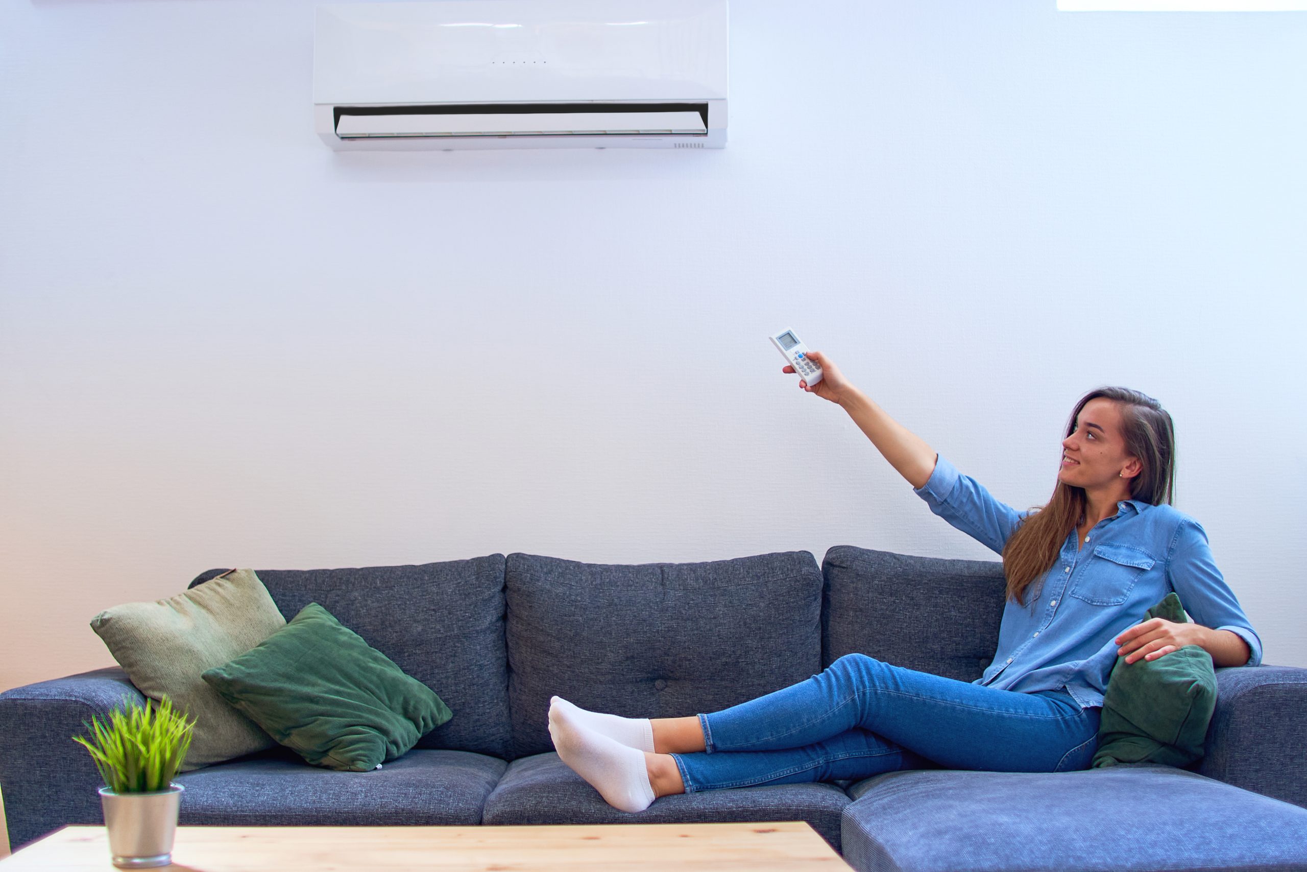 Young happy woman sitting on couch under air conditioner and adj
